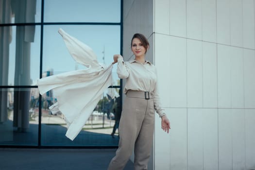 Playful fashion business woman in stylish beige pant suit standing near office building and confidently look at camera, copy space.