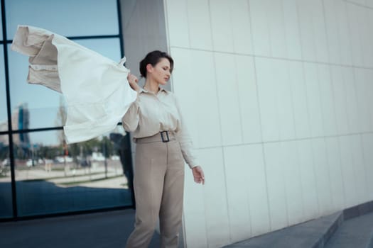 Portrait of a beautiful young successful business woman in beige pant suit standing against office district, copy space.