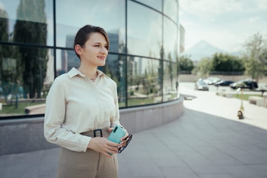 Woman outdoor portrait in business office style with phone in hand in the city streets.