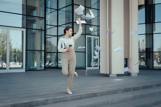 Young woman runs out of an office building scattering paperwork at the end of a workday before vacation.