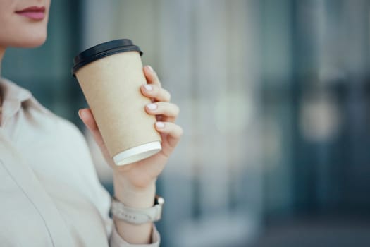 Close-up side view of unrecognizable young business woman holding in hands paper cup with takeaway coffee or other beverage.