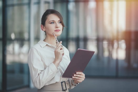 Caucasian business woman with a tablet and a stylus in her hands thought about promising business projects near office building, copy space.