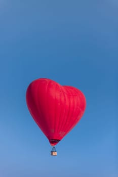 Hot air balloon in the shape of a red heart against a clear blue sky, a journey of lovers on a honeymoon, copy space, vertical.