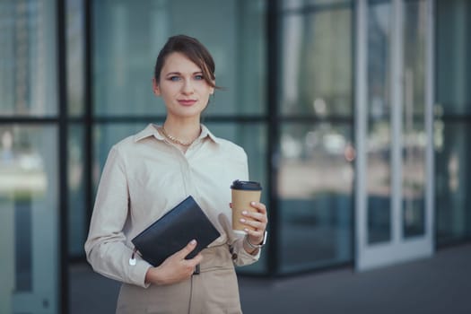 Young caucasian woman left the office for a coffee break with a notepad and coffee in a paper cup.