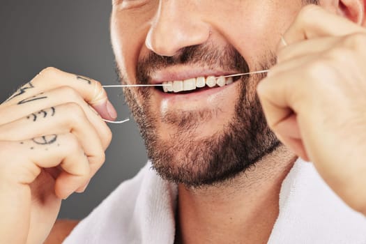 Floss, dental hygiene and man cleaning teeth, for wellness and against grey studio background. Oral health, healthy male and thin filaments string for fresh breath, remove plaque and mouth healthcare.
