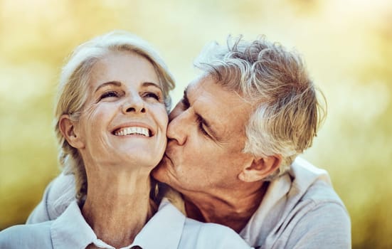 Senior couple, kiss and cheek with smile for love, romance and embrace together in the nature outdoors. Happy elderly woman and man kissing face for romantic bonding or quality time in happiness.