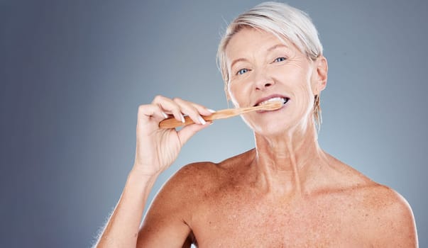 Brushing teeth, portrait and senior woman in studio for dental, mouth and tooth wellness with product marketing, advertising and promotion space. Elderly model with toothbrush for morning care mockup.