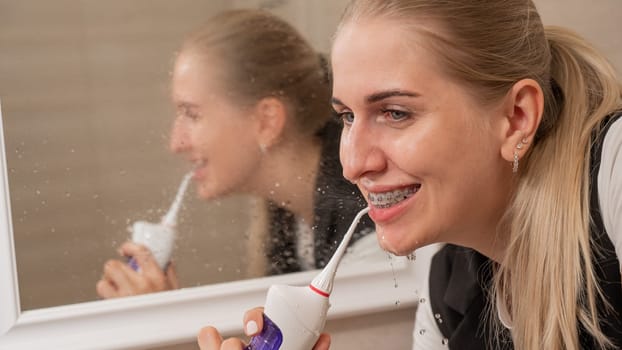 A woman with braces on her teeth uses an irrigator. Close-up portrait