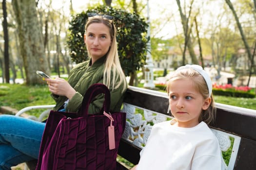 Young mother and small daughter sitting on the bench in park portrait