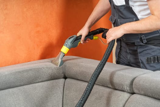 Dry cleaner's man employee removing dirt from furniture in flat, closeup, vacuum clean sofa with professional equipment. cleaning sofa with washing suction cleaner closeup.