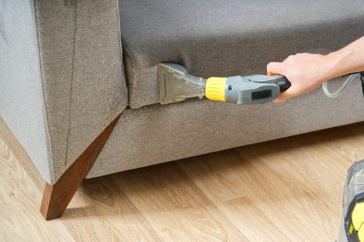 Dry cleaner's man employee removing dirt from furniture in flat, closeup, vacuum clean sofa with professional equipment. cleaning sofa with washing suction cleaner closeup.