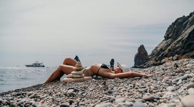 Woman bilds stones pyramid on the seashore on a sunny day on the blue sea background. Happy holidays. Pebble beach, calm sea, travel destination. Concept of happy vacation on the sea, meditation, spa