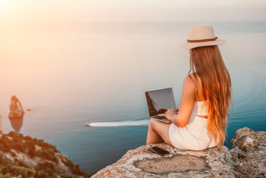 Digital nomad, Business woman working on laptop by the sea. Pretty lady typing on computer by the sea at sunset, makes a business transaction online from a distance. Freelance, remote work on vacation