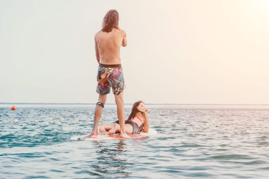 Sea woman and man on sup. Silhouette of happy young woman and man, surfing on SUP board, confident paddling through water surface. Idyllic sunset. Active lifestyle at sea or river