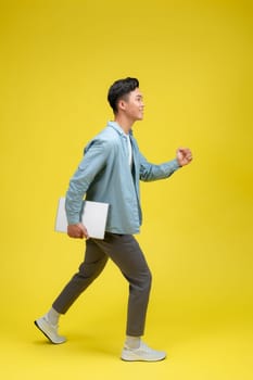 young man happy positive smile go walk hold laptop meeting isolated over yellow color background