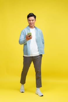 portrait of smiling young casual guy using mobile phone, walking isolated over yellow background