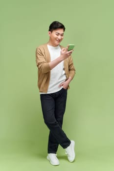 Attractive man chatting or typing text message using cell phone isolated over green background