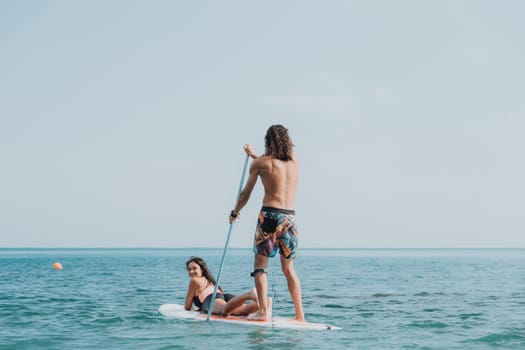 Sea woman and man on sup. Silhouette of happy young woman and man, surfing on SUP board, confident paddling through water surface. Idyllic sunset. Active lifestyle at sea or river