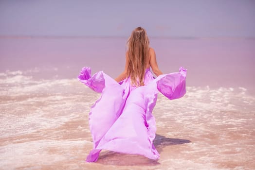 Woman pink salt lake. Against the backdrop of a pink salt lake, a woman in a long pink dress takes a leisurely stroll along the white, salty shore, capturing a wanderlust moment