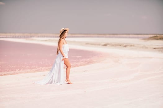 Woman in pink salt lake. She in a white dress and hat enjoys the scenic view of a pink salt lake as she walks along the white, salty shore, creating a lasting memory