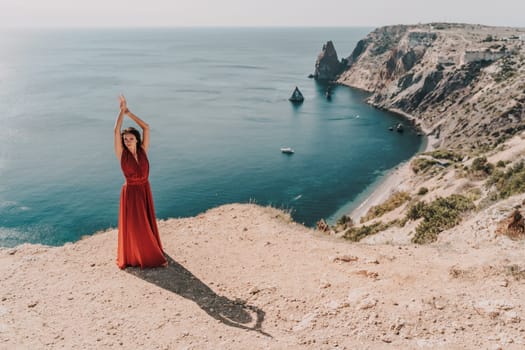 Woman red dress sea. posing on a rocky outcrop high above the sea. Girl on the nature on blue sky background. Fashion photo