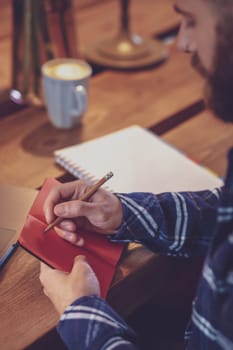 Cropped image of casual business man or freelancer planning his work on notebook, working on laptop computer with smart phone, cup of coffee on table at coffee shop or home office, working from cafe concept