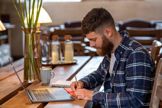 Casual business man or freelancer planning his work on notebook, working on laptop computer with smart phone, cup of coffee on table at coffee shop or home office, working from cafe concept