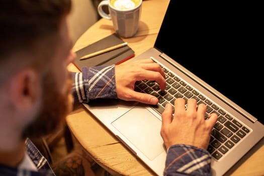 Young man drinking coffee in cafe and using laptop. Man's hands using laptop during coffee break. Working from cafe concept