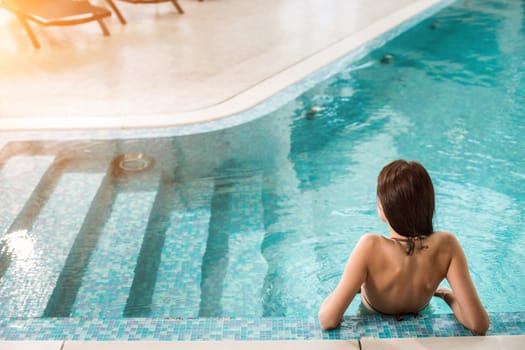 Beautiful long hair female model posing by the pool in wellness spa hotel resort.