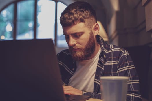 Young professional surfing the Internet on his laptop with cup of coffee on table at coffee shop or home office, working from cafe concept