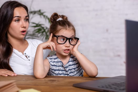 Irritated mother watching at the mistakes her daughter's homework on a laptop. Emotions.