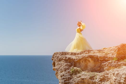 Woman yellow dress sea. Side view Young beautiful sensual woman in yellow long dress posing on a rock high above the sea at sunset. Girl in nature against the blue sky.