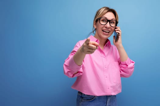 young surprised caucasian blonde secretary woman with ponytail hairstyle, glasses and pink shirt chatting on the phone.