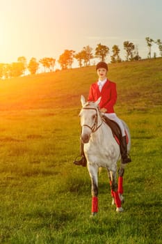 Young woman rider, wearing red redingote and white breeches, with her horse in evening sunset light. Outdoor photography in lifestyle mood