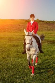 Young woman rider, wearing red redingote and white breeches, with her horse in evening sunset light. Outdoor photography in lifestyle mood