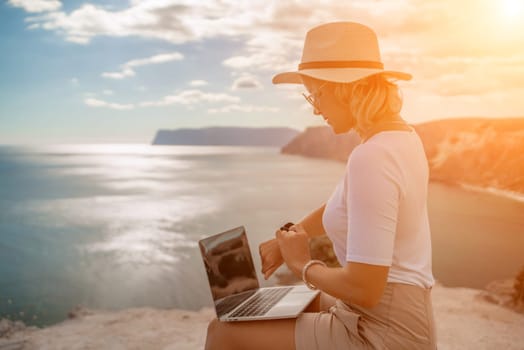 Freelance women sea working on the computer. Good looking middle aged woman typing on a laptop keyboard outdoors with a beautiful sea view. The concept of remote work