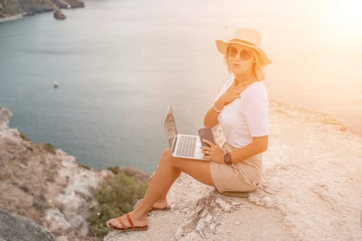 Freelance women sea working on the computer. Good looking middle aged woman typing on a laptop keyboard outdoors with a beautiful sea view. The concept of remote work