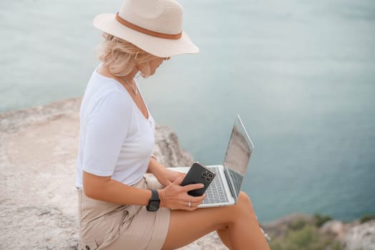 Freelance women sea working on the computer. Good looking middle aged woman typing on a laptop keyboard outdoors with a beautiful sea view. The concept of remote work