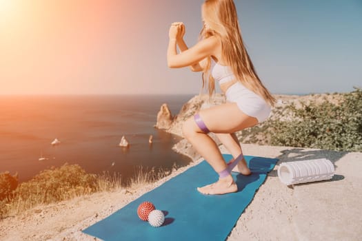 Middle aged well looking woman with black hair doing Pilates with the ring on the yoga mat near the sea on the pebble beach. Female fitness yoga concept. Healthy lifestyle, harmony and meditation.