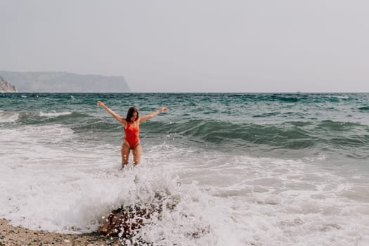 Woman travel sea. Young Happy woman in a long red dress posing on a beach near the sea on background of volcanic rocks, like in Iceland, sharing travel adventure journey