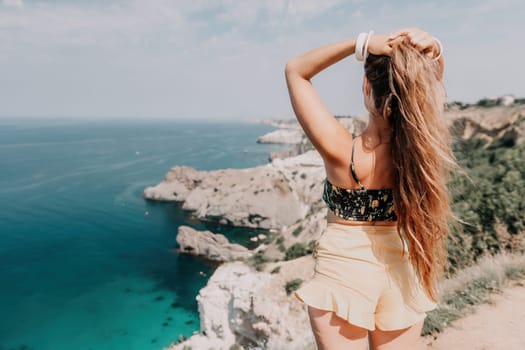 Woman travel sea. Happy tourist taking picture outdoors for memories. Woman traveler looks at the edge of the cliff on the sea bay of mountains, sharing travel adventure journey.