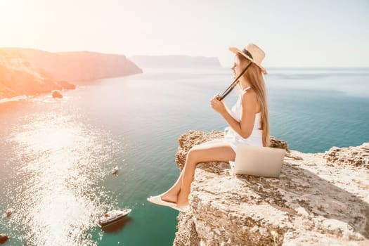 Digital nomad, Business woman working on laptop by the sea. Pretty lady typing on computer by the sea at sunset, makes a business transaction online from a distance. Freelance, remote work on vacation