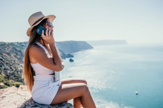 Successful business woman in yellow hat working on laptop by the sea. Pretty lady typing on computer at summer day outdoors. Freelance, travel and holidays concept.