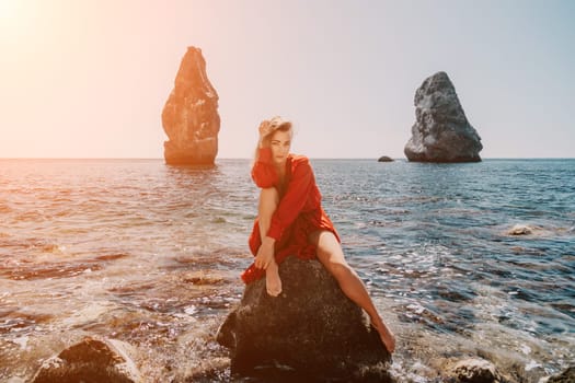 Woman travel sea. Young Happy woman in a long red dress posing on a beach near the sea on background of volcanic rocks, like in Iceland, sharing travel adventure journey