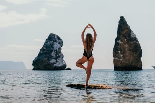 Woman meditating in yoga pose silhouette at the ocean, beach and rock mountains. Motivation and inspirational fit and exercising. Healthy lifestyle outdoors in nature, fitness concept.