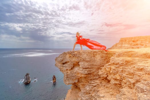 woman red silk dress stands by the ocean, with mountains in the background, as her dress sways in the breeze