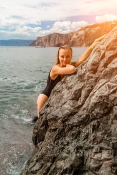 Woman travel sea. Attractive blonde woman in a black swimsuit enjoying the sea air on the seashore around the rocks. Travel and vacation concept