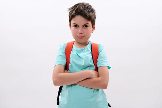 Portrait of a sad, distressed, offended preteen boy, tearful school kid with arms folded, feeling sadness after act of bullying at school, looking at camera, isolated on white studio background