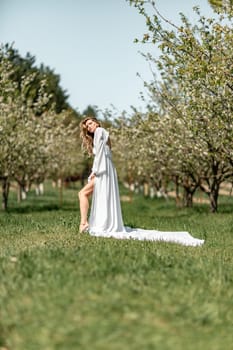 Blond blooming garden. A woman in a white dress walks through a blossoming cherry orchard. Long dress flies to the sides