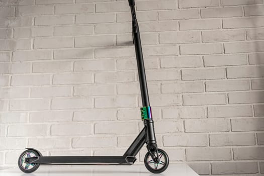 Side view of a stunt scooter with rainbow-colored wheels against a light brick wall. equipment for extreme skating in a skatepark and on a ramp. Details of the scooter. Repair, rental and sale of scooters